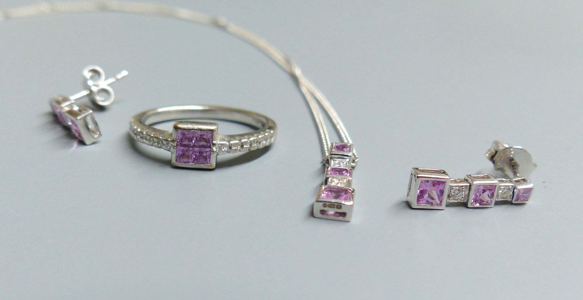 A modern 18ct white gold, pink sapphire and diamond set line pendant, on 18ct white gold chain & a pair of matching earrings